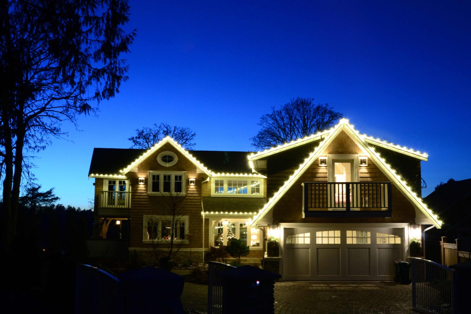 Two-story shingled home lit with warm white C9 roofline bulbs at blue hour
