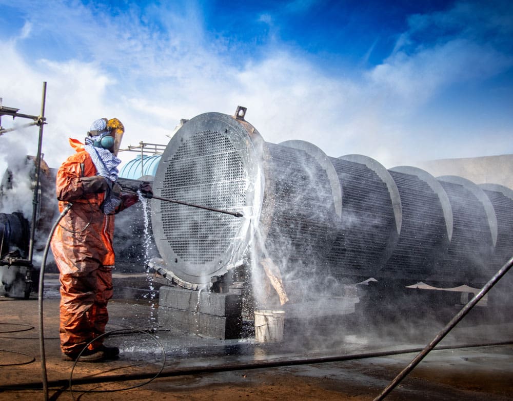 A worker spraying a large pipe with water.